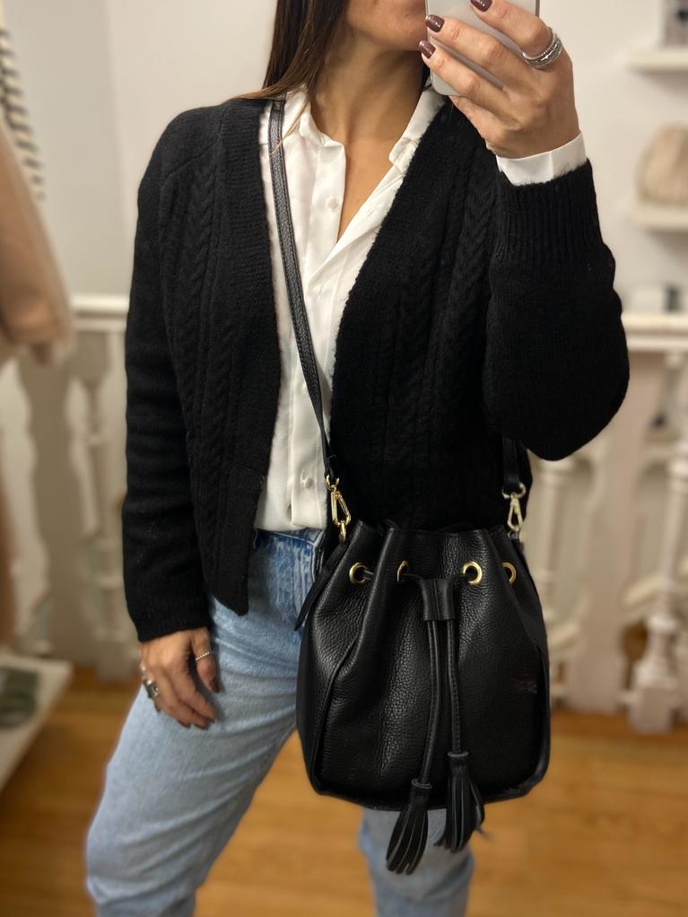 Pessoa com cardigan preto, camisa branca e calças de ganga segurando bolsa preta de couro