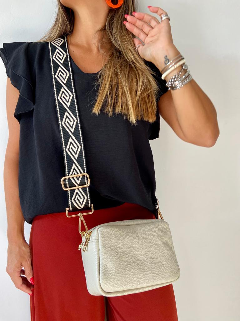 Mulher com blusa preta, calças vermelhas e bolsa de couro branco com alça preta e branca