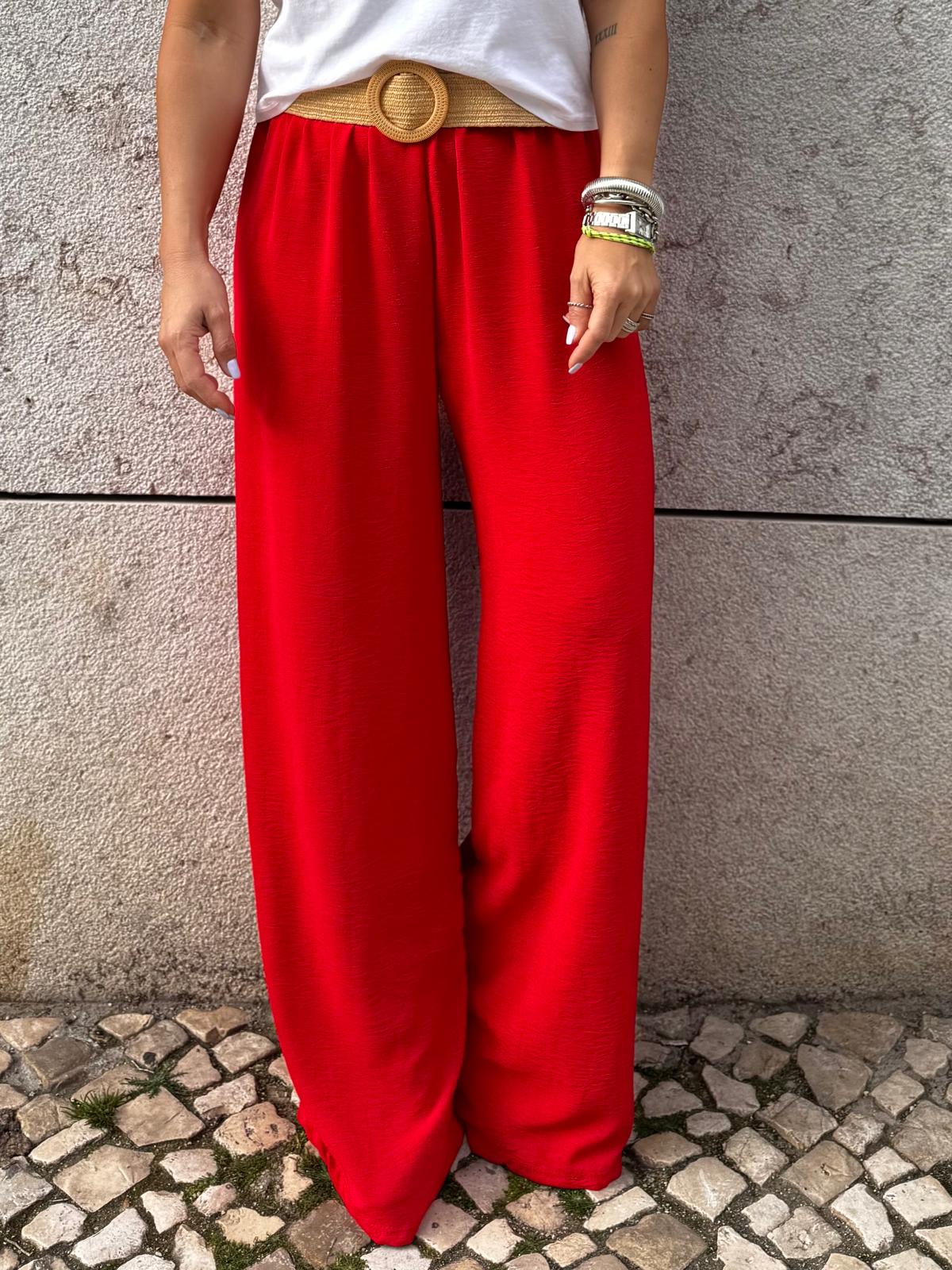 Calças largas vermelhas, cinto de ráfia bege, fundo de parede cinza e calçada portuguesa
