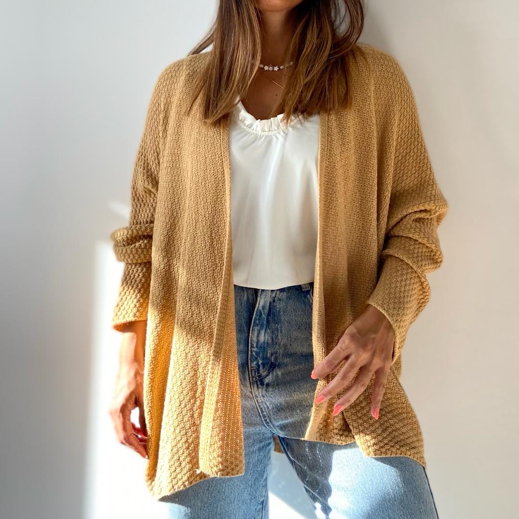 Cardigan bege de malha usado com camisola branca e calças de ganga em fundo branco
