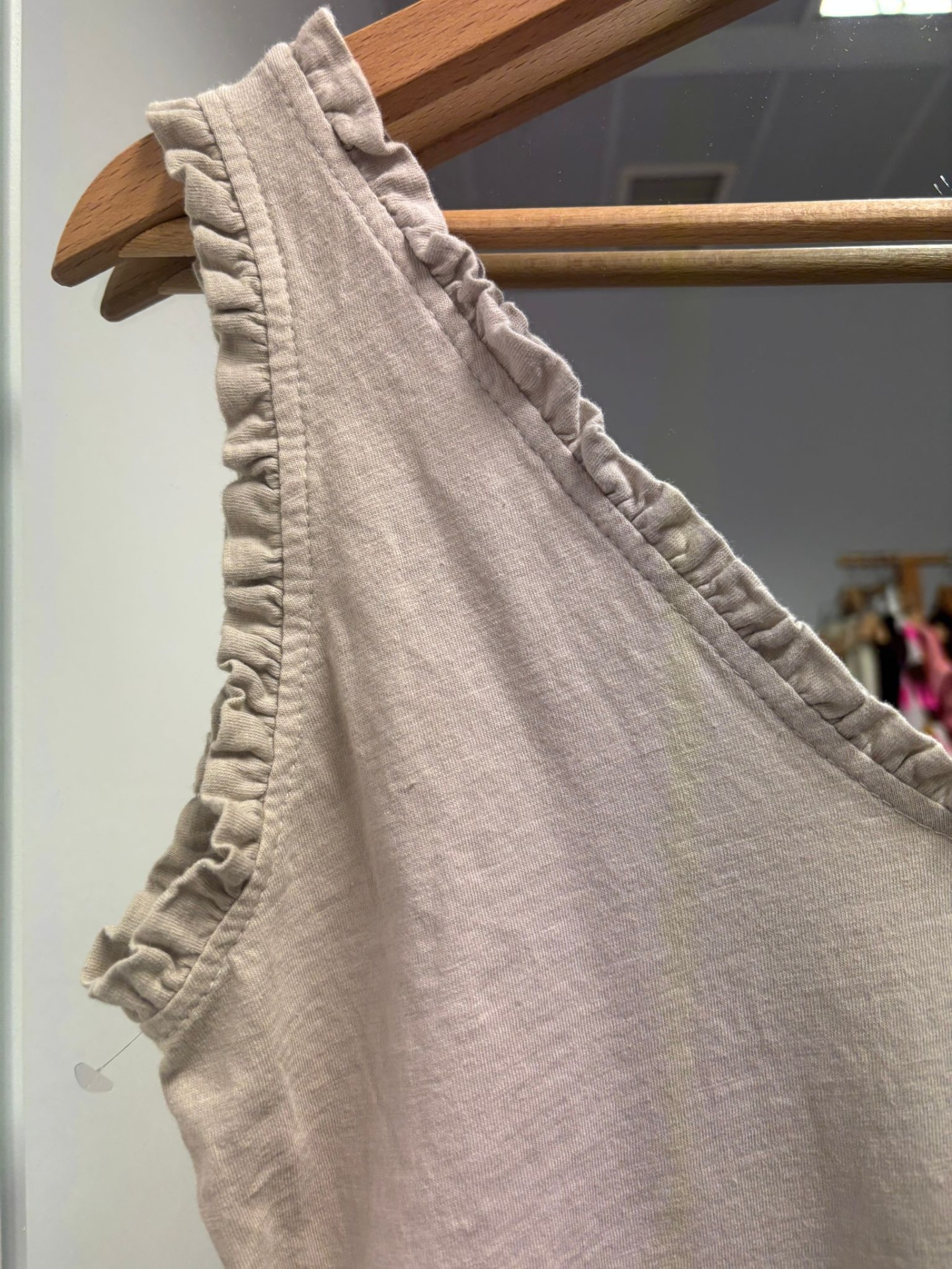Peça de roupa bege claro com alças franzidas pendurada num cabide de madeira.