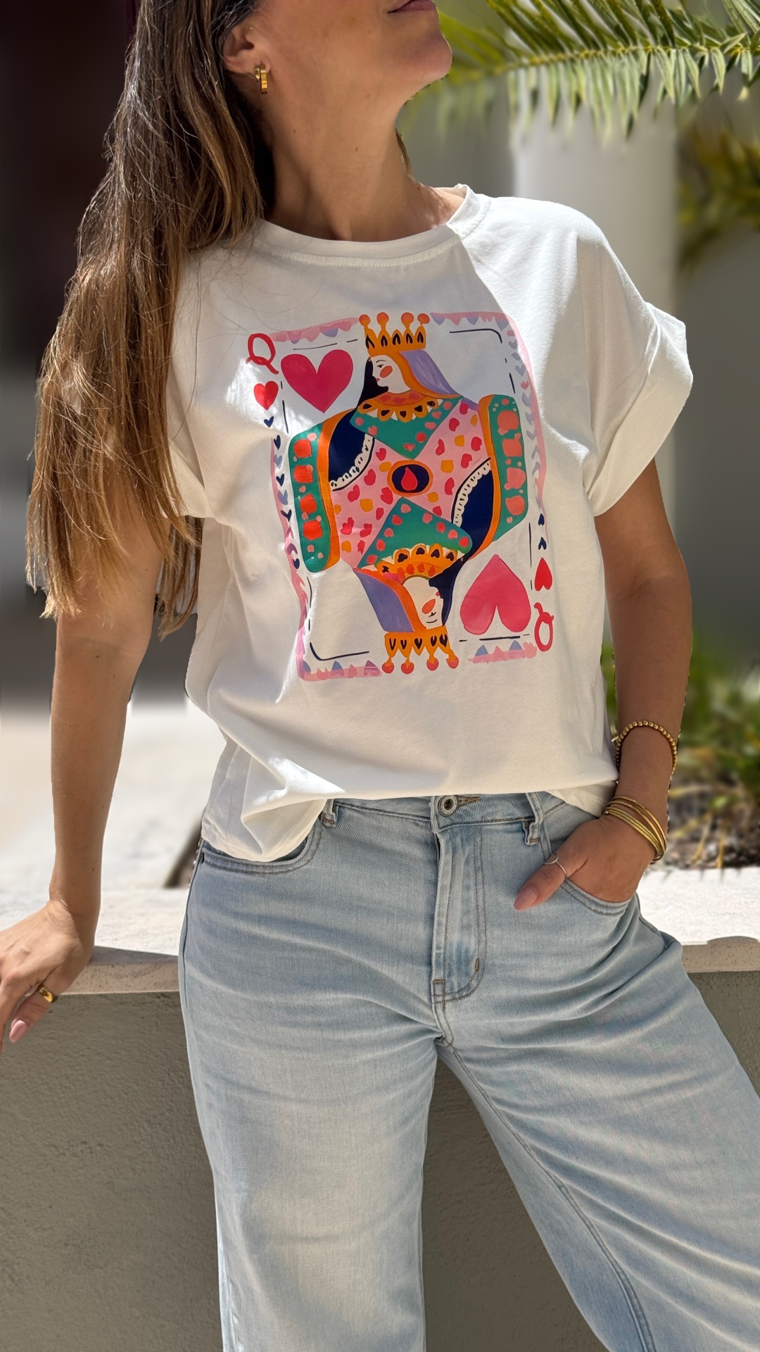 T-shirt branca com estampa colorida da carta Rainha de Copas usando calças de ganga claras