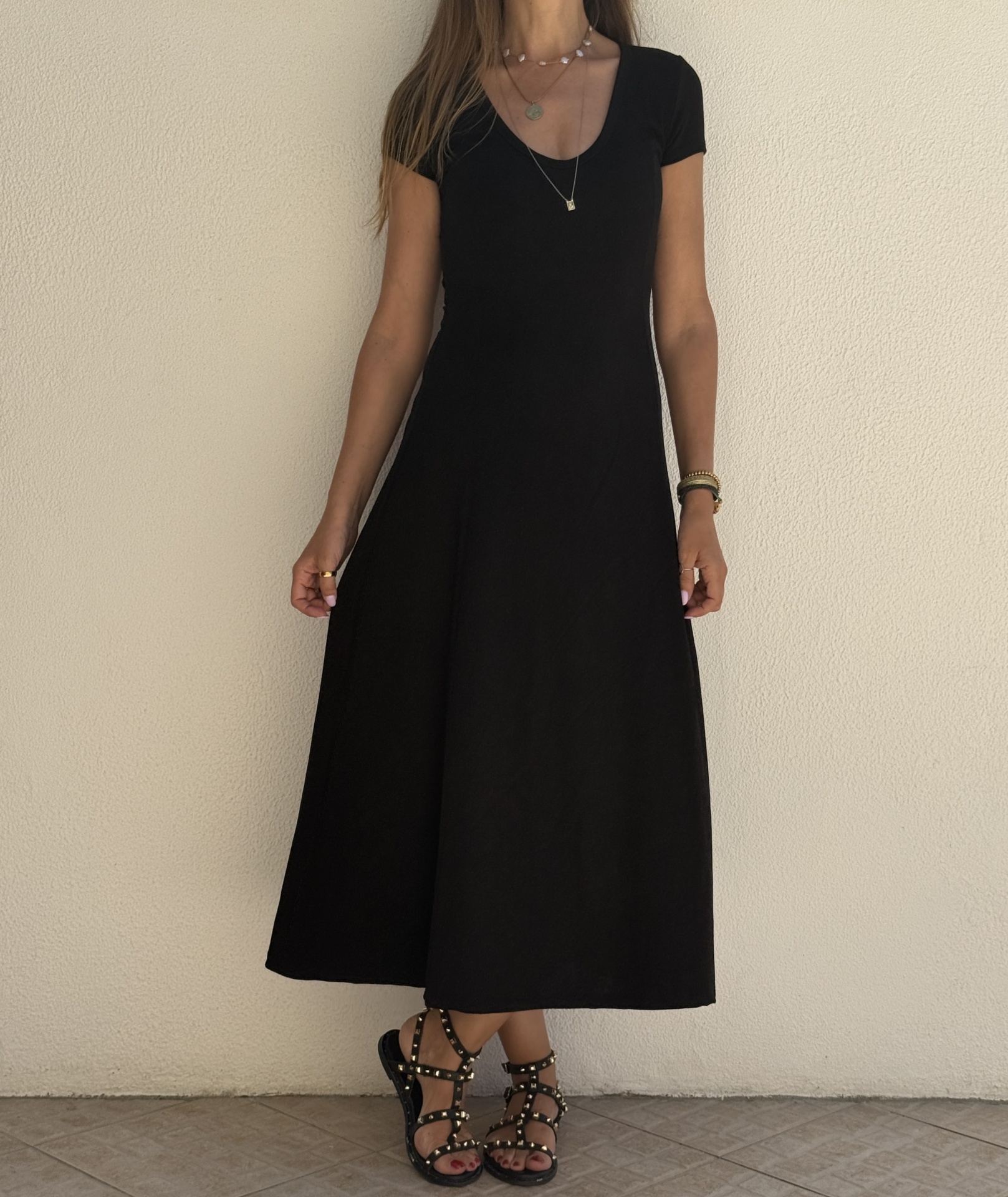 Vestido preto de manga curta com decote em V usado por mulher com sandálias pretas e tachas douradas