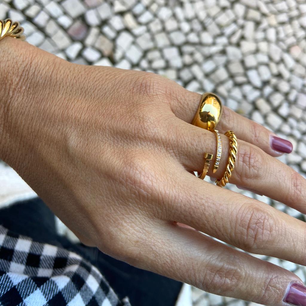 Mão com três anéis dourados e unhas pintadas cor vinho sobre calçada de pedras