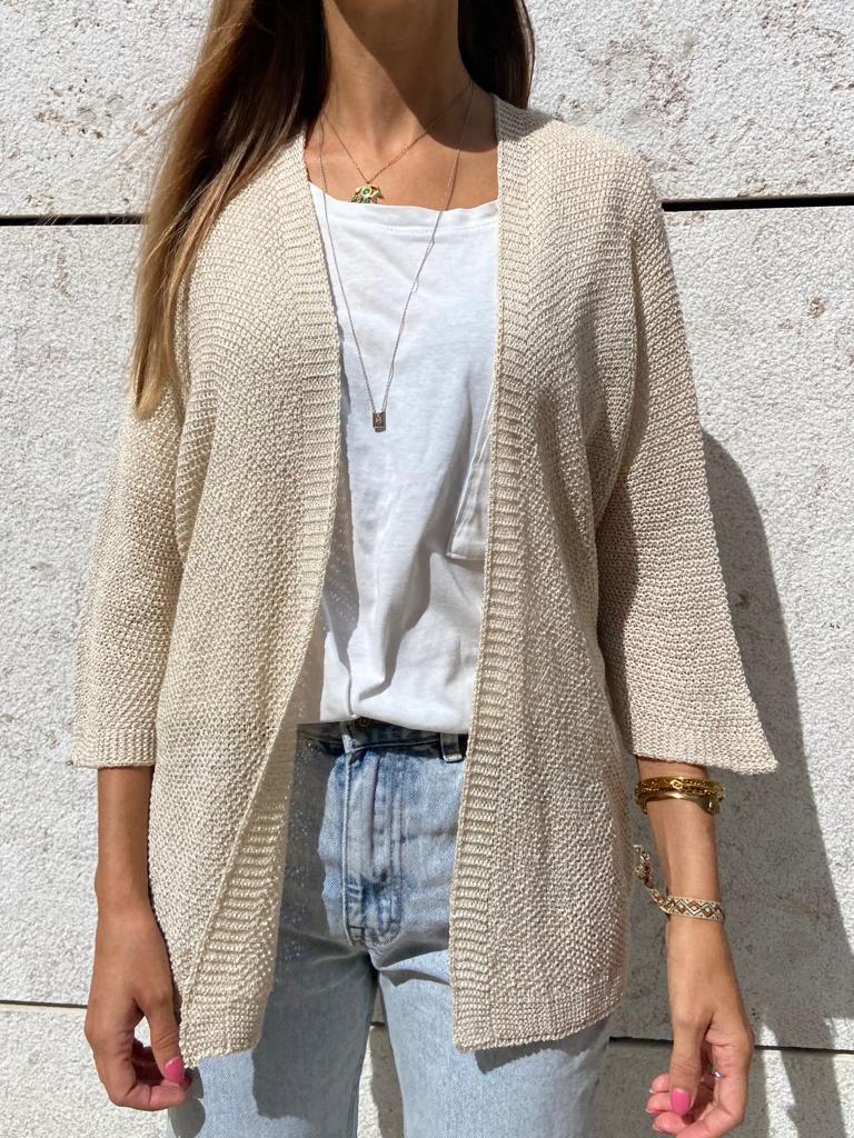 Casaco de malha bege com manga 3/4 sobre t-shirt branca e calças de ganga azuis