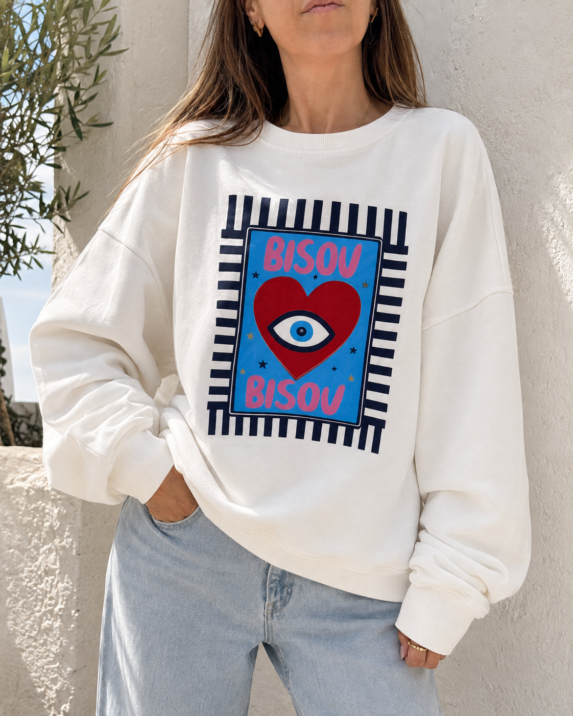 Sweatshirt branca com design colorido com o texto BISOU BISOU e um coração com um olho no centro