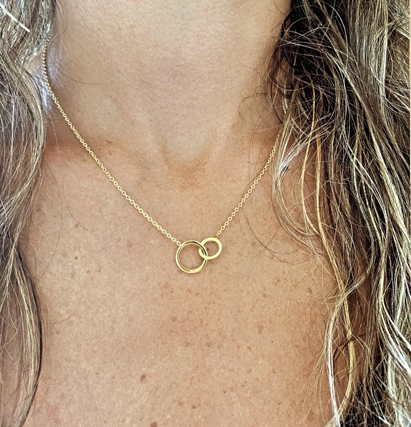 Colar dourado com dois anéis entrelaçados no pescoço