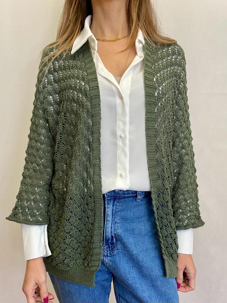 Cardigan verde aberto com padrão vazado sobre camisa branca e calças de ganga azuis