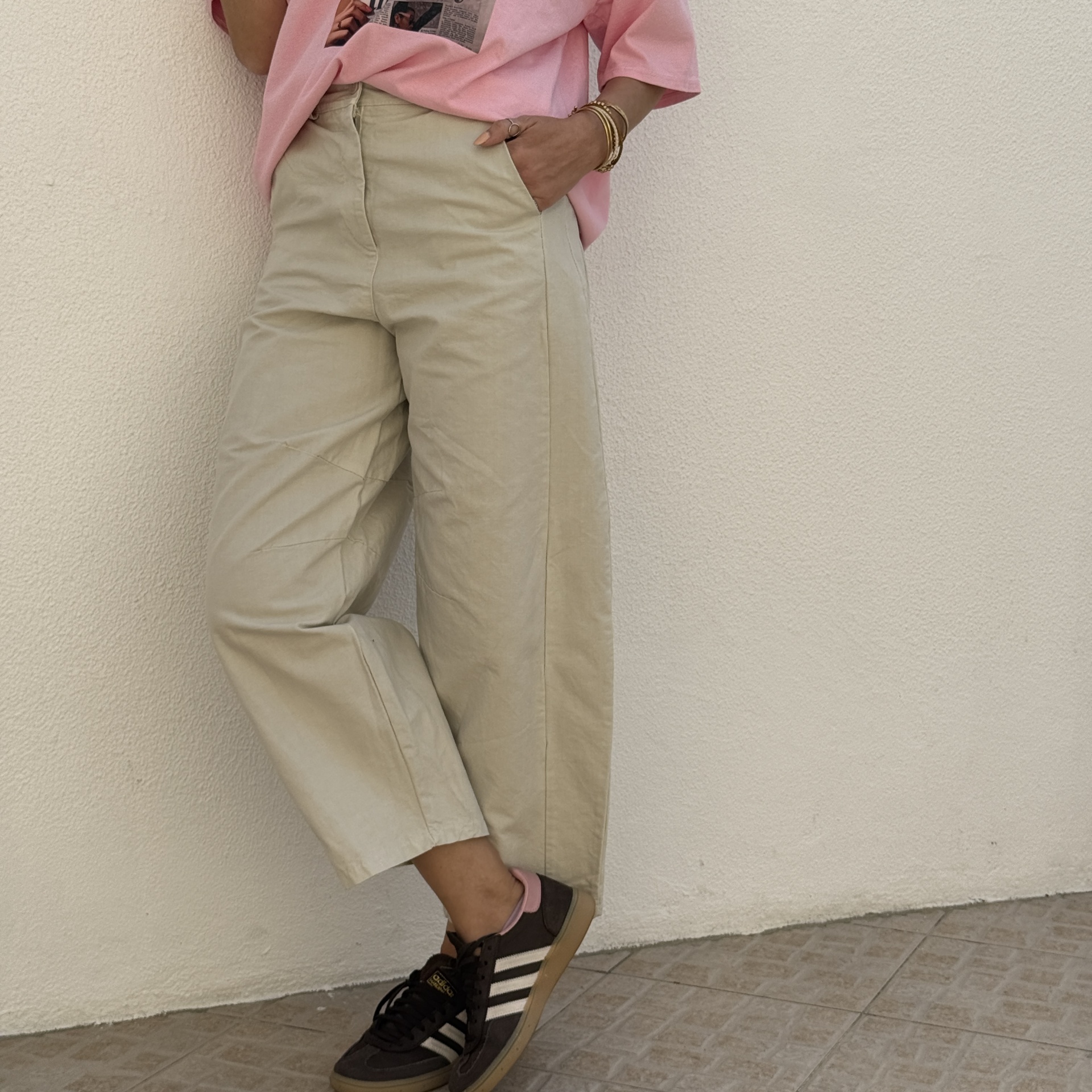 Calças bege com ténis Adidas pretos e t-shirt rosa com estampa de jornal