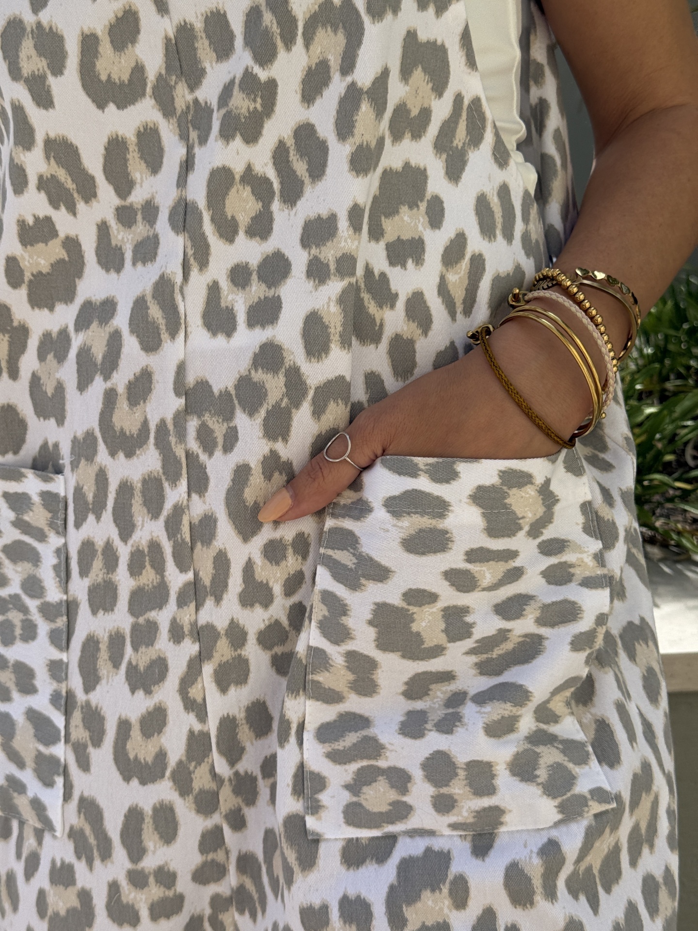 Peça de roupa com padrão animal print bege e cinza, mão feminina com pulseiras e anel no bolso.