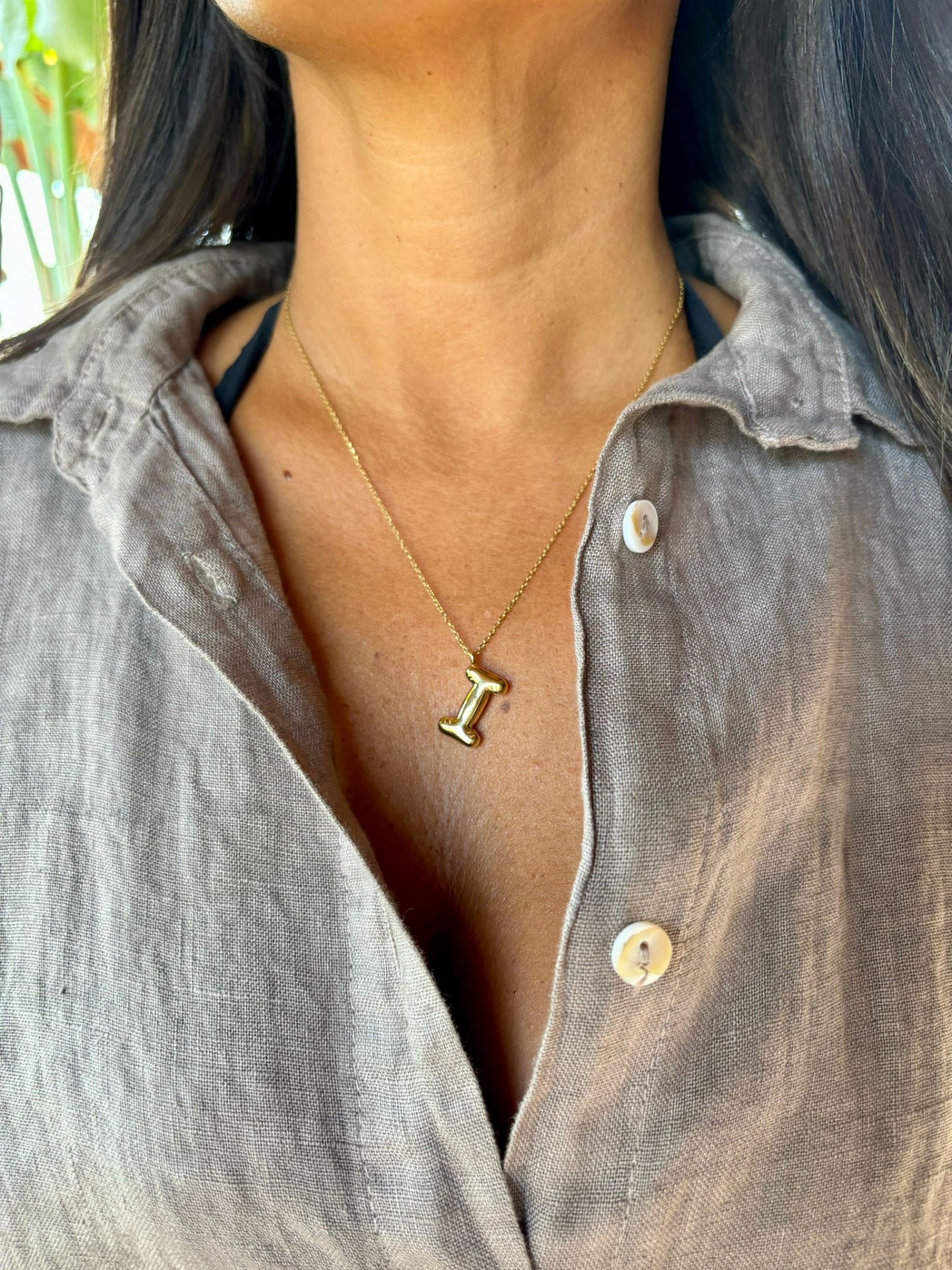 Colar dourado com pendente da letra I e camisa de linho bege.