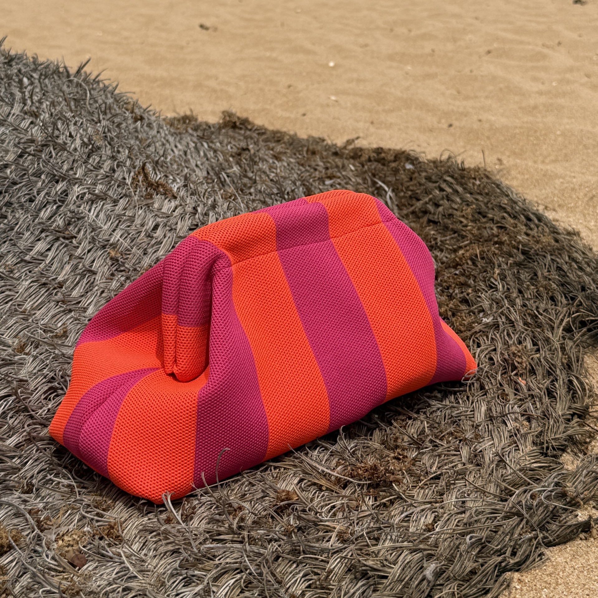 Bolsa rosa e laranja às riscas sobre fibras naturais e areia