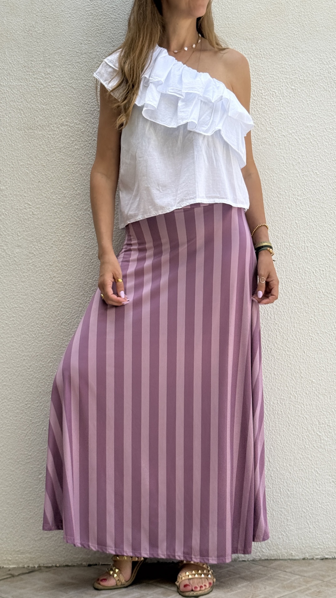 Blusa branca com folhos num ombro e saia roxa às riscas verticais