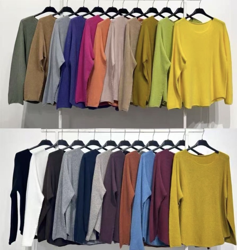 Camisolas de malha coloridas penduradas em cabides num suporte branco