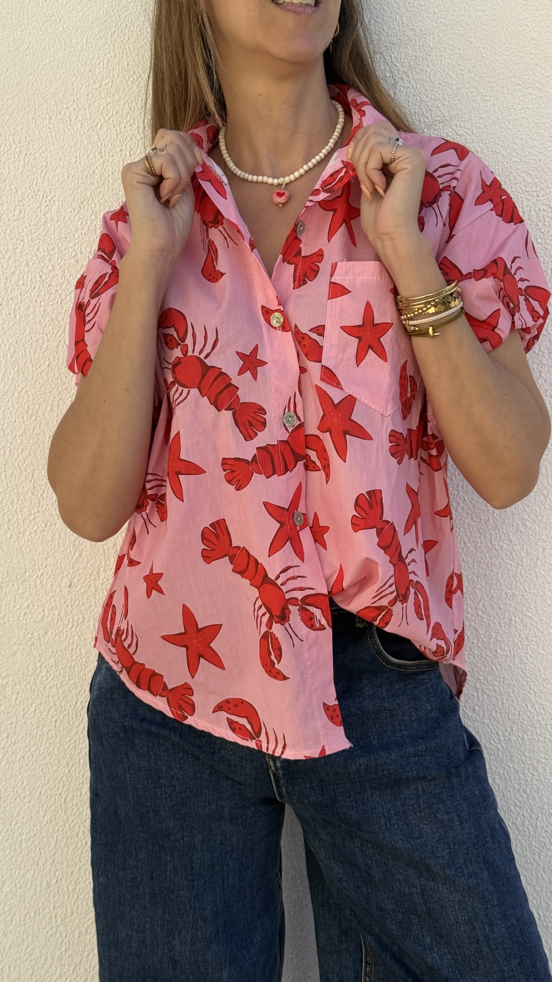 Camisa rosa com lagostas vermelhas e estrelas do mar, com calças de ganga azul.