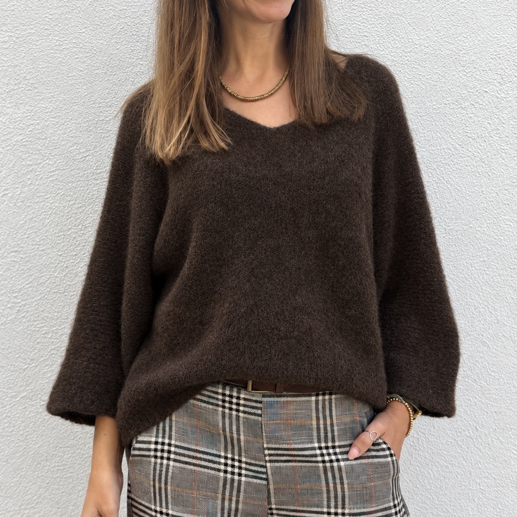Mulher com camisola castanha de malha e calças xadrez cinza/bege, fundo branco