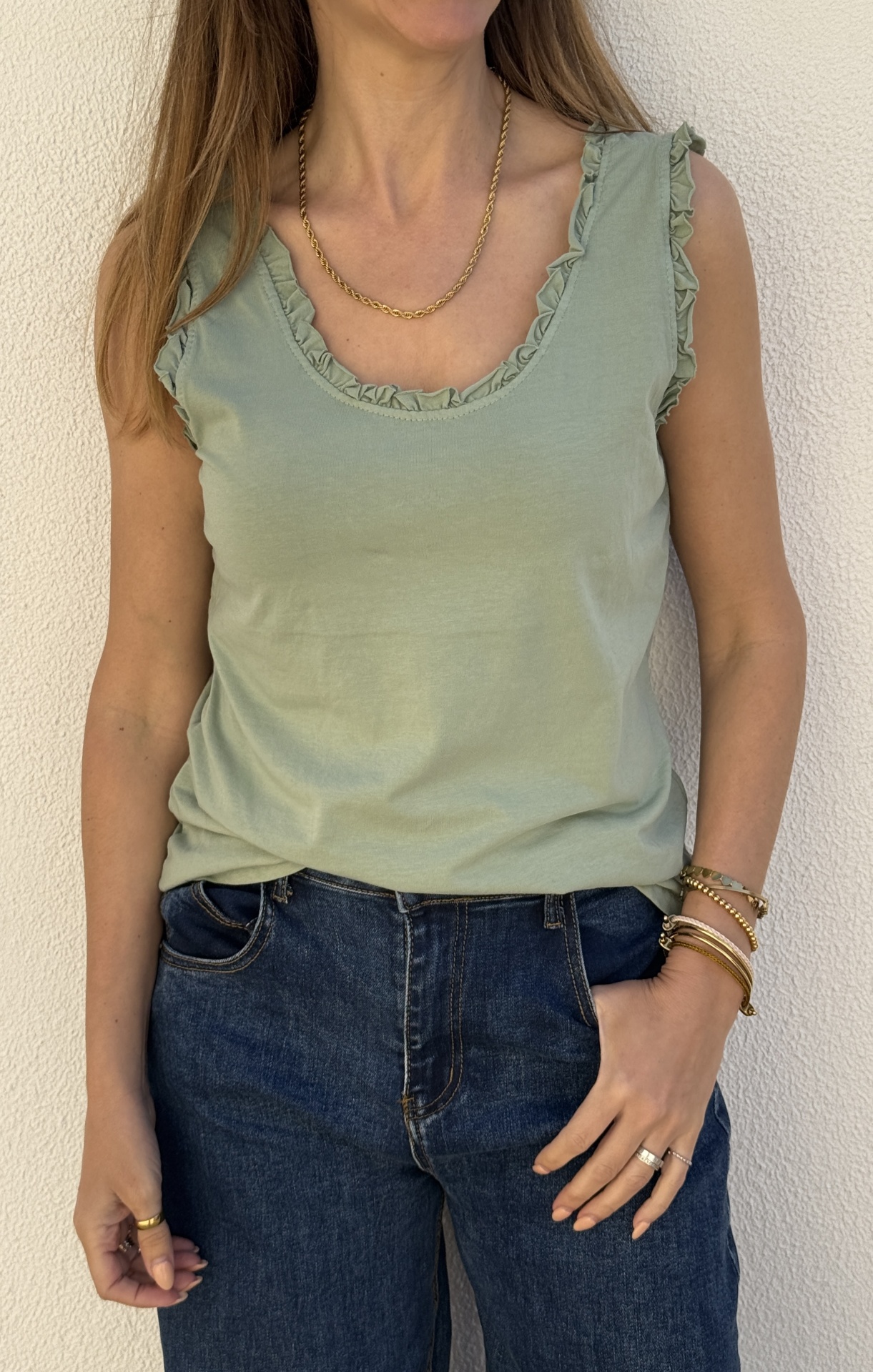 Top verde claro com folhos e jeans azul escuro usados por mulher com acessórios dourados