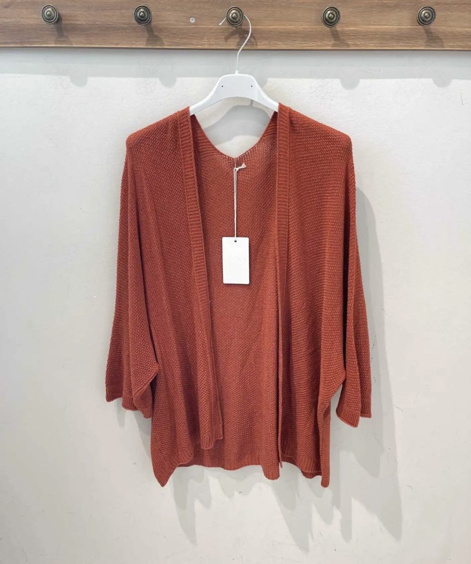 Casaco de malha laranja pendurado num cabide branco numa parede branca com cabideiro de madeira