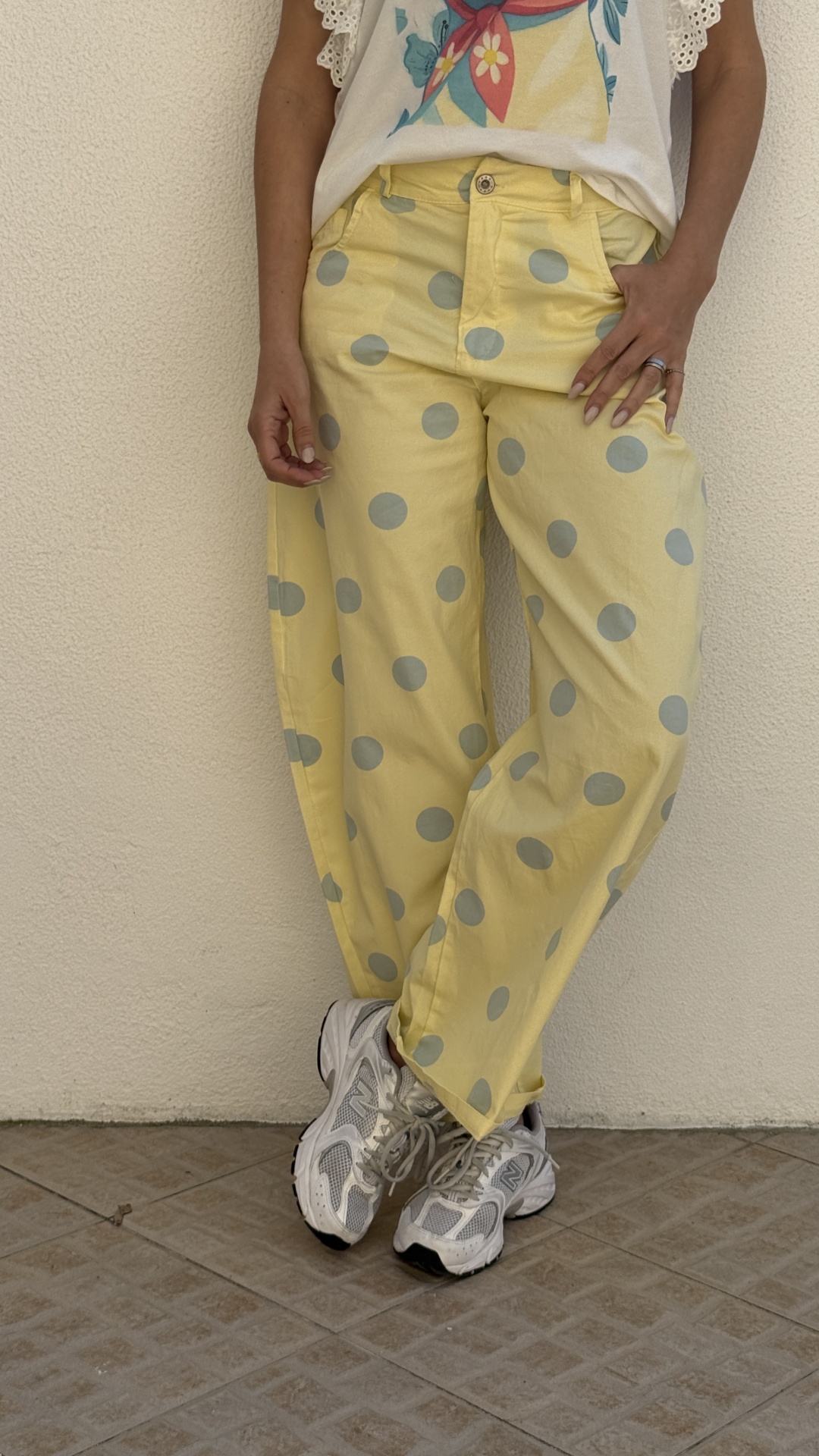 Calças amarelas com bolinhas cinzentas usadas com ténis brancos junto a uma parede clara.