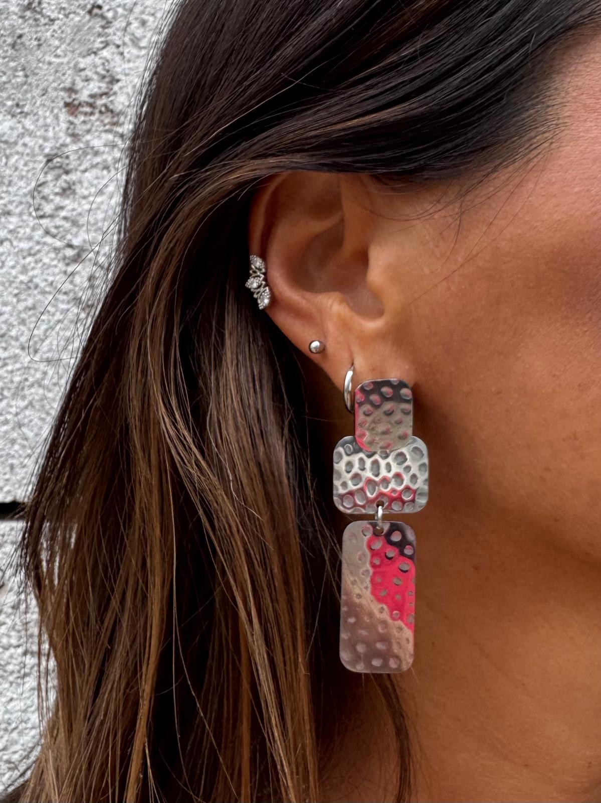 Brinco pendente metálico martelado em tons prateados e vermelhos na orelha direita