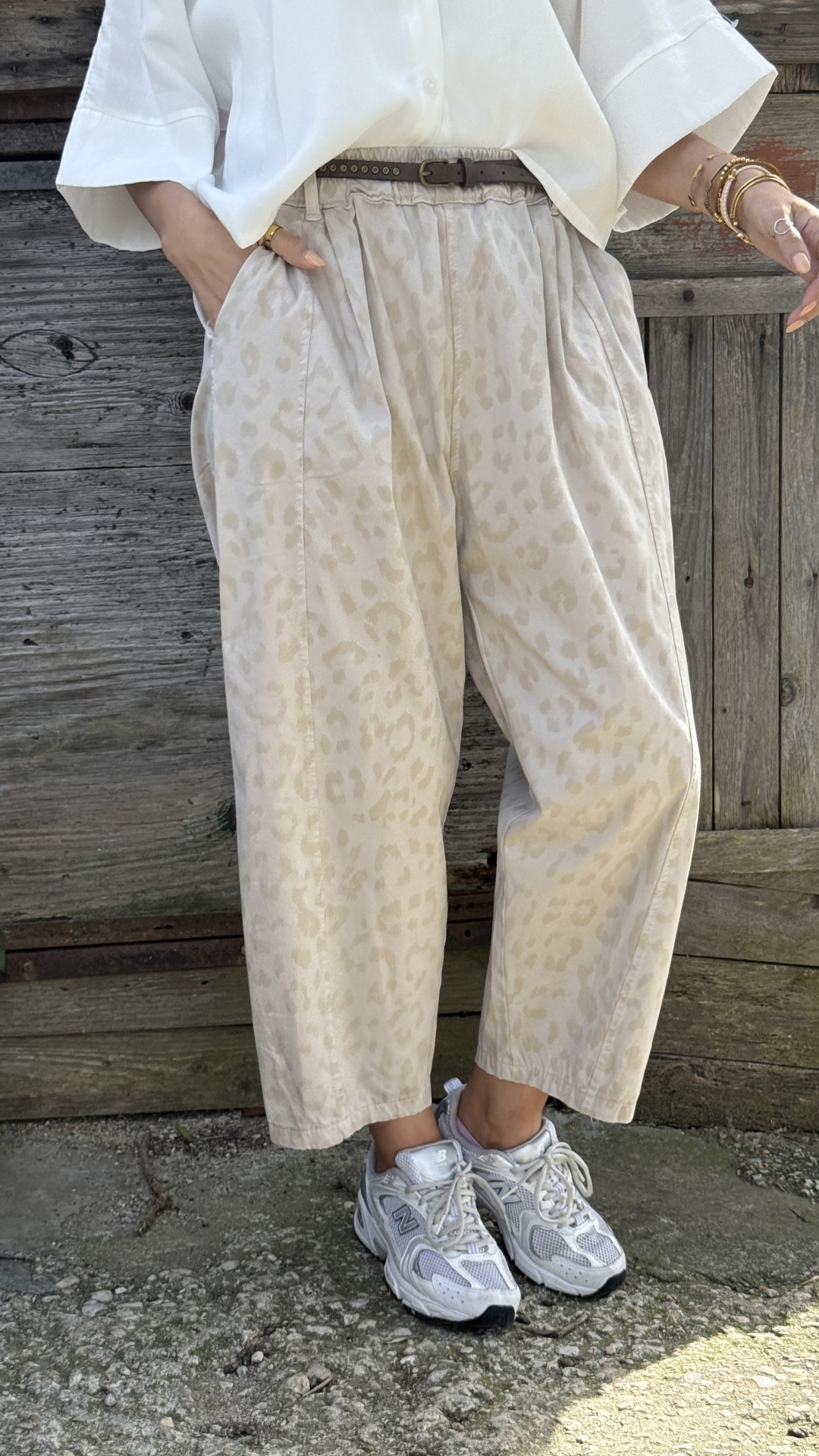 Calças largas bege com padrão de manchas e sapatilhas desportivas brancas em chão de pedra