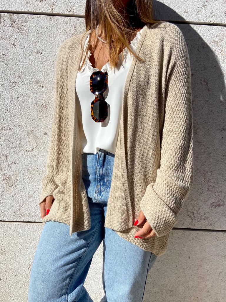 Mulher com camisola bege de malha, camisa branca e calças de ganga azuis