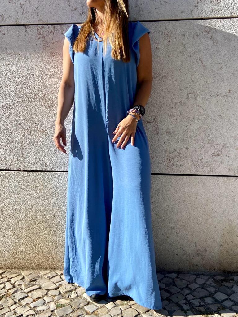 Mulher usando macacão azul claro sem mangas em parede de pedra clara