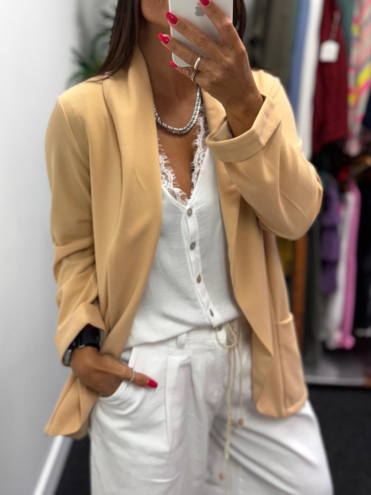 Blazer bege com camisa branca rendada e calças brancas em ambiente interno