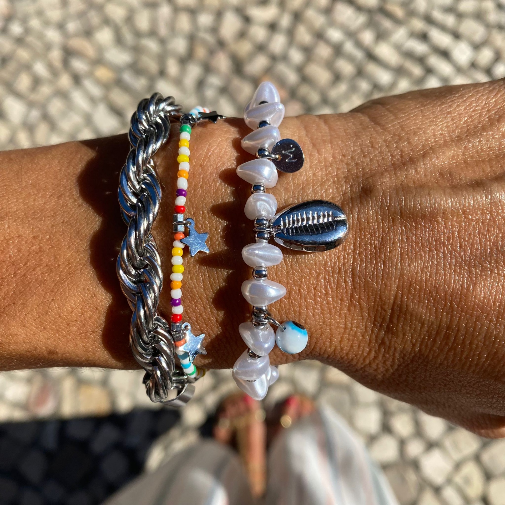 Três pulseiras variadas no pulso de uma pessoa com pele morena