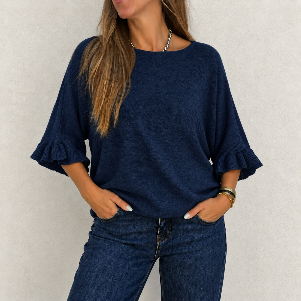 Blusa azul escuro com manga 3/4 e folho, usada com calças azul escuro e acessórios de pulso.