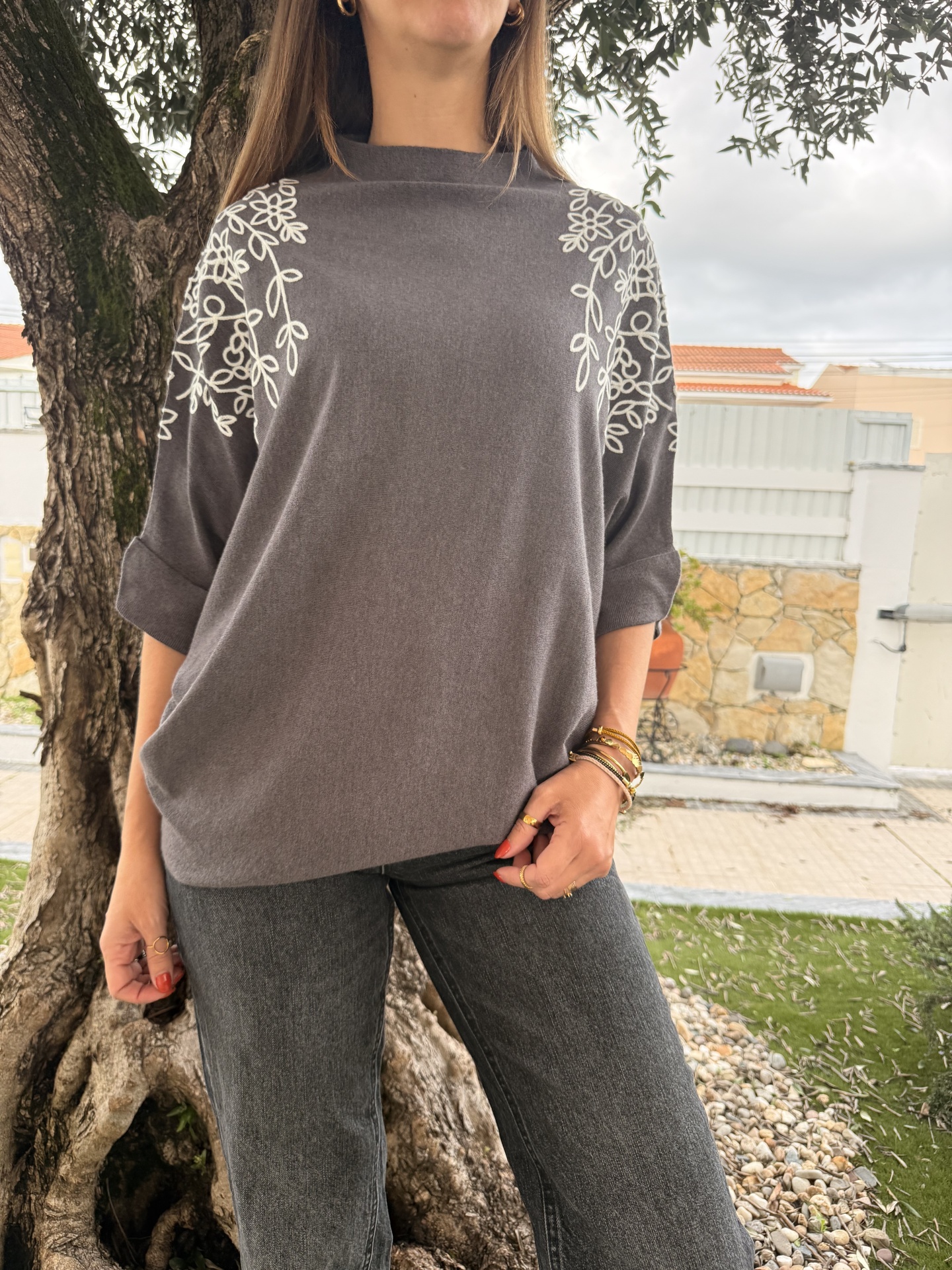 Casaco cinza com padrão floral branco nos ombros e mangas enroladas.