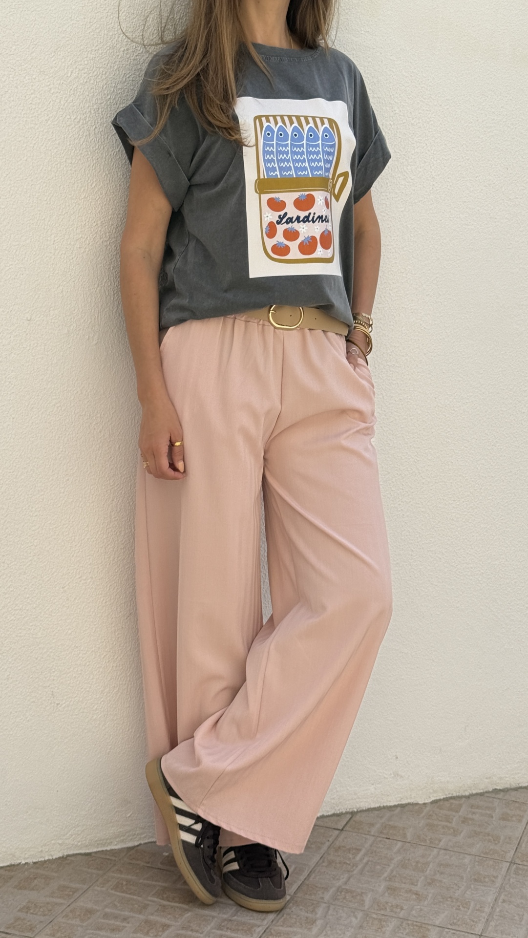 Mulher com t-shirt cinzenta estampada, calças rosas largas e sapatilhas pretas