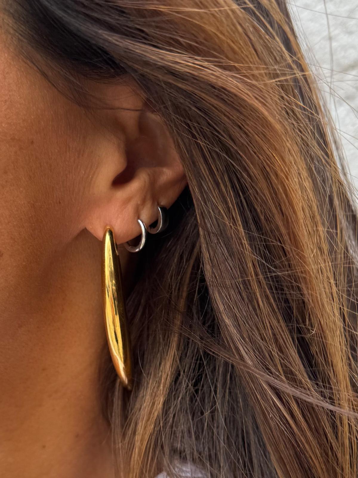 Três brincos em orelha feminina, dois pequenos prateados e um grande dourado brilhante