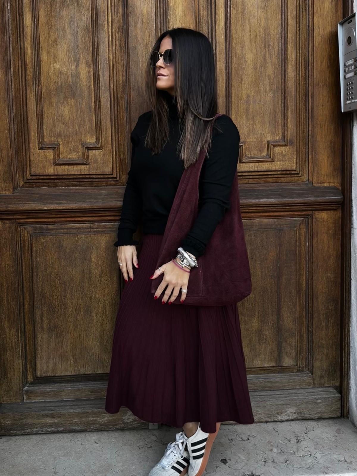 Mulher com roupa preta e vinho em frente a porta de madeira