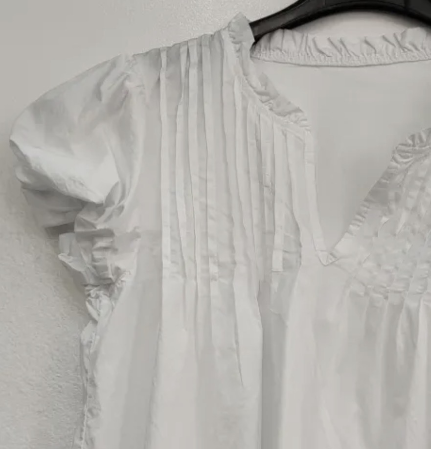 Blusa branca com pregas e gola em V pendurada em cabide