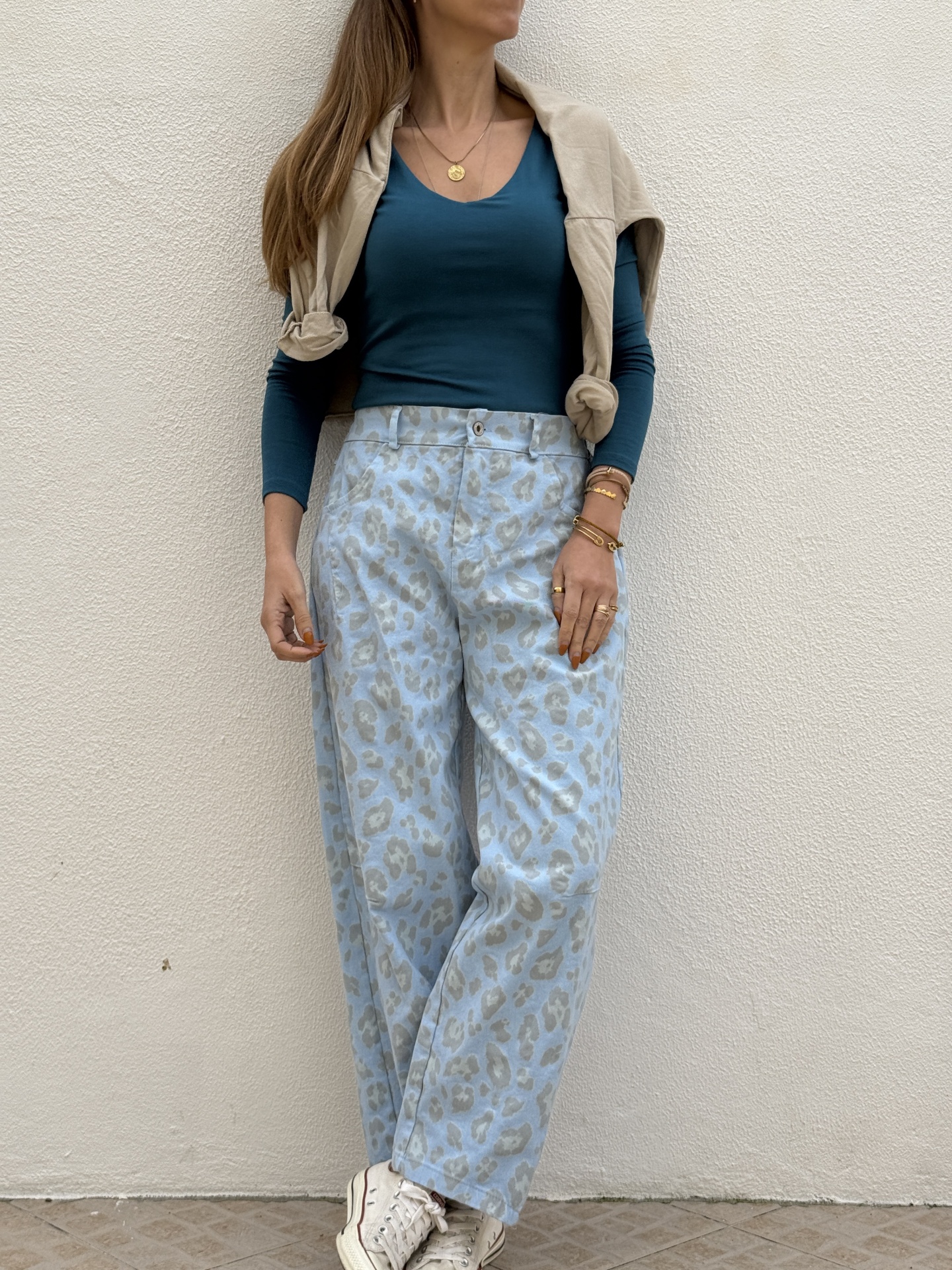 Mulher com camisola azul escura, calças largas bege com padrão animal print e sapatilhas brancas