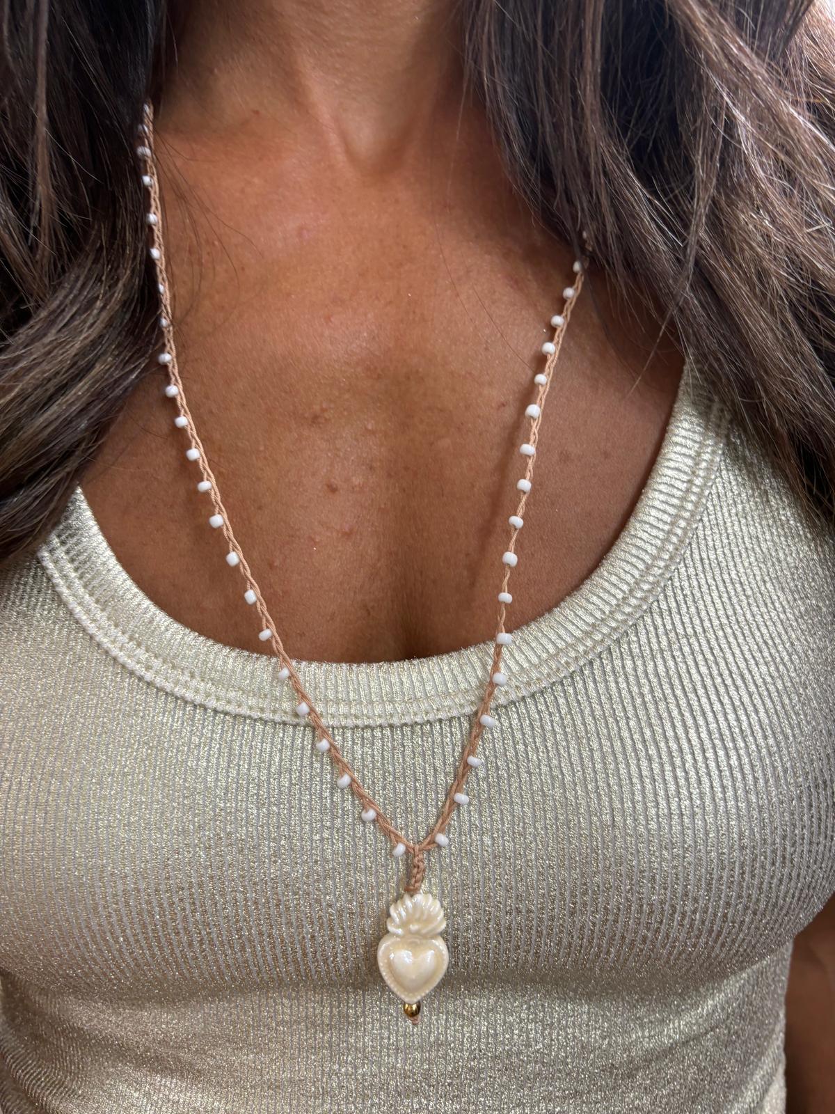 Colar com pequenas pérolas e pendente de coração branco sobre camiseta bege