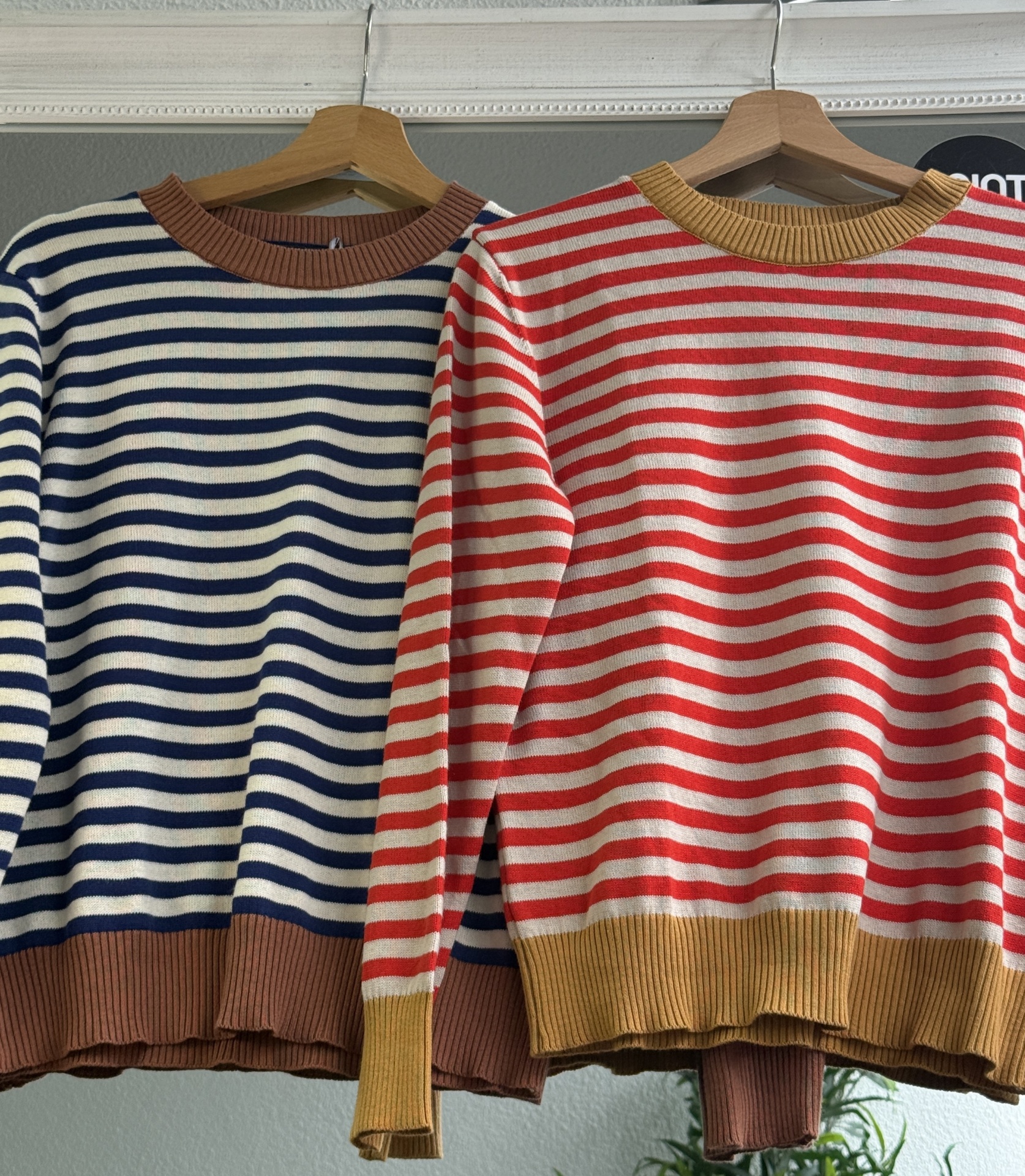 Dois suéteres de riscas coloridas pendurados em cabides de madeira