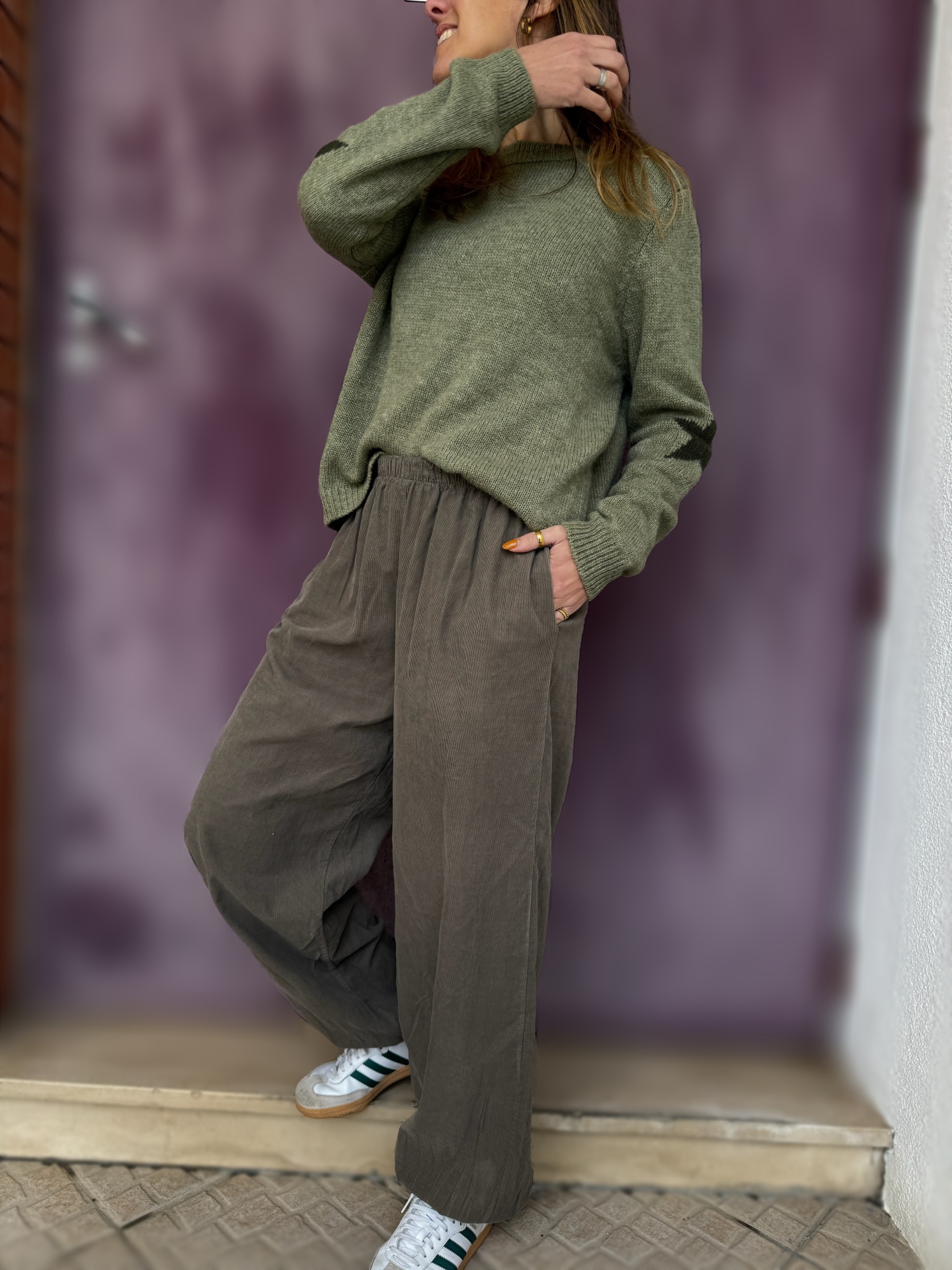 Pessoa a vestir camisola verde de malha e calças cinzentas largas com ténis brancos