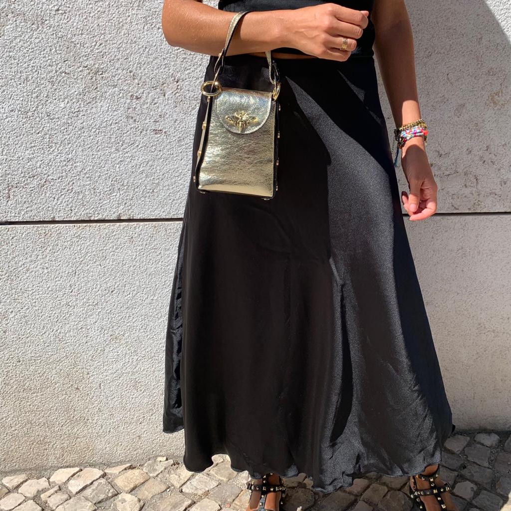 Vestido preto comprido com mala dourada e pulseiras coloridas
