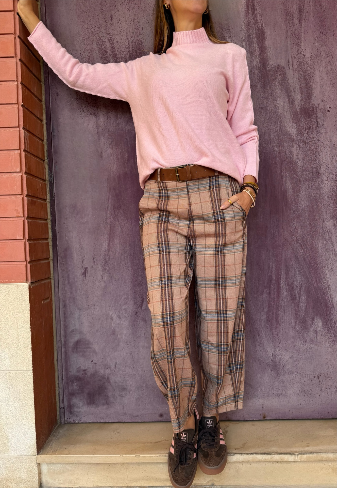 Pessoa com camisola rosa, calças aos quadrados e sapatilhas Adidas