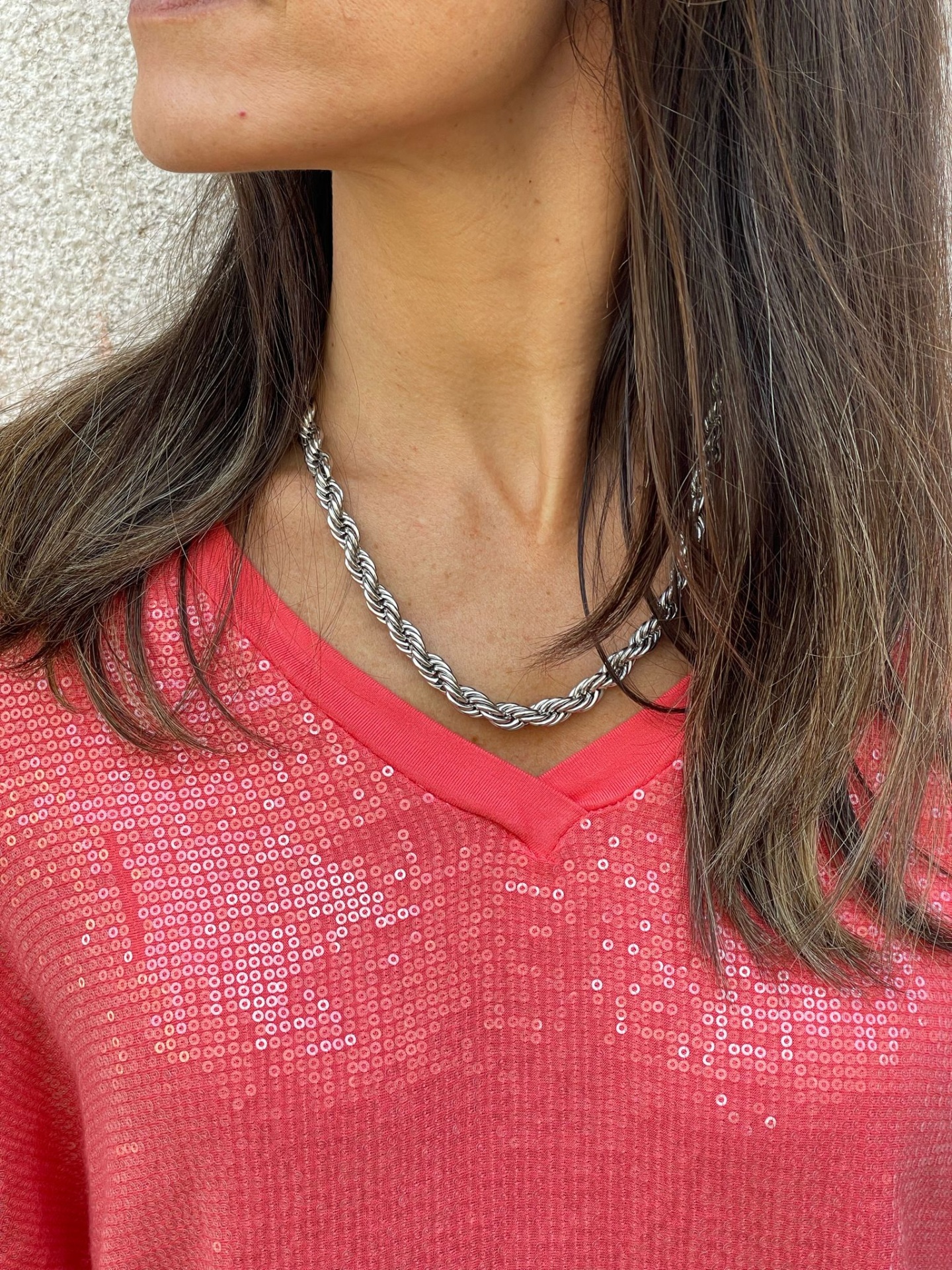 Colar prateado com corrente entrelaçada no pescoço de mulher com camisa vermelha de lantejoulas