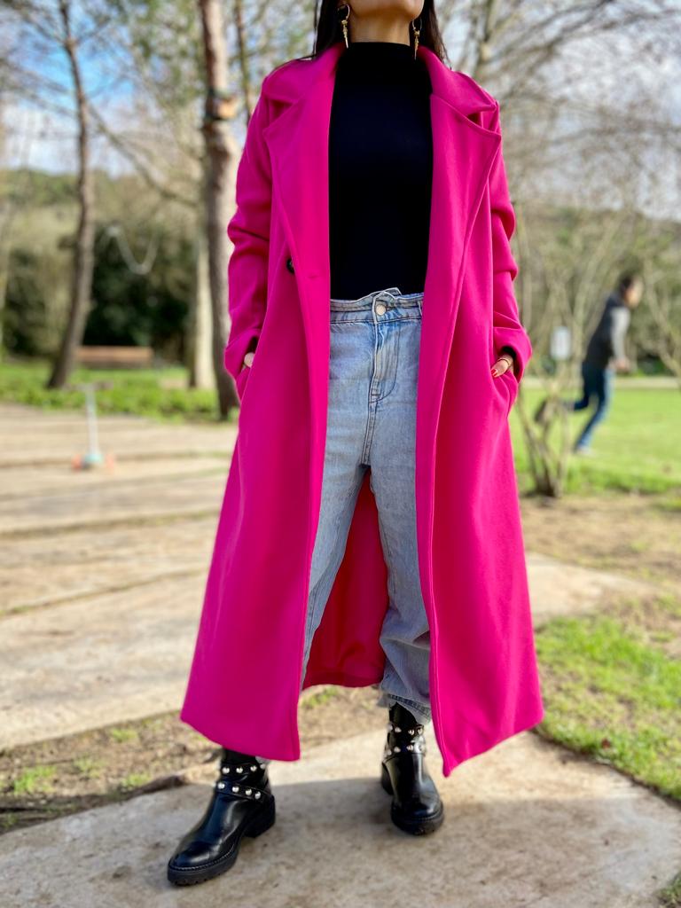 casaco rosa choque comprido, camisola preta, calças de ganga e botas pretas