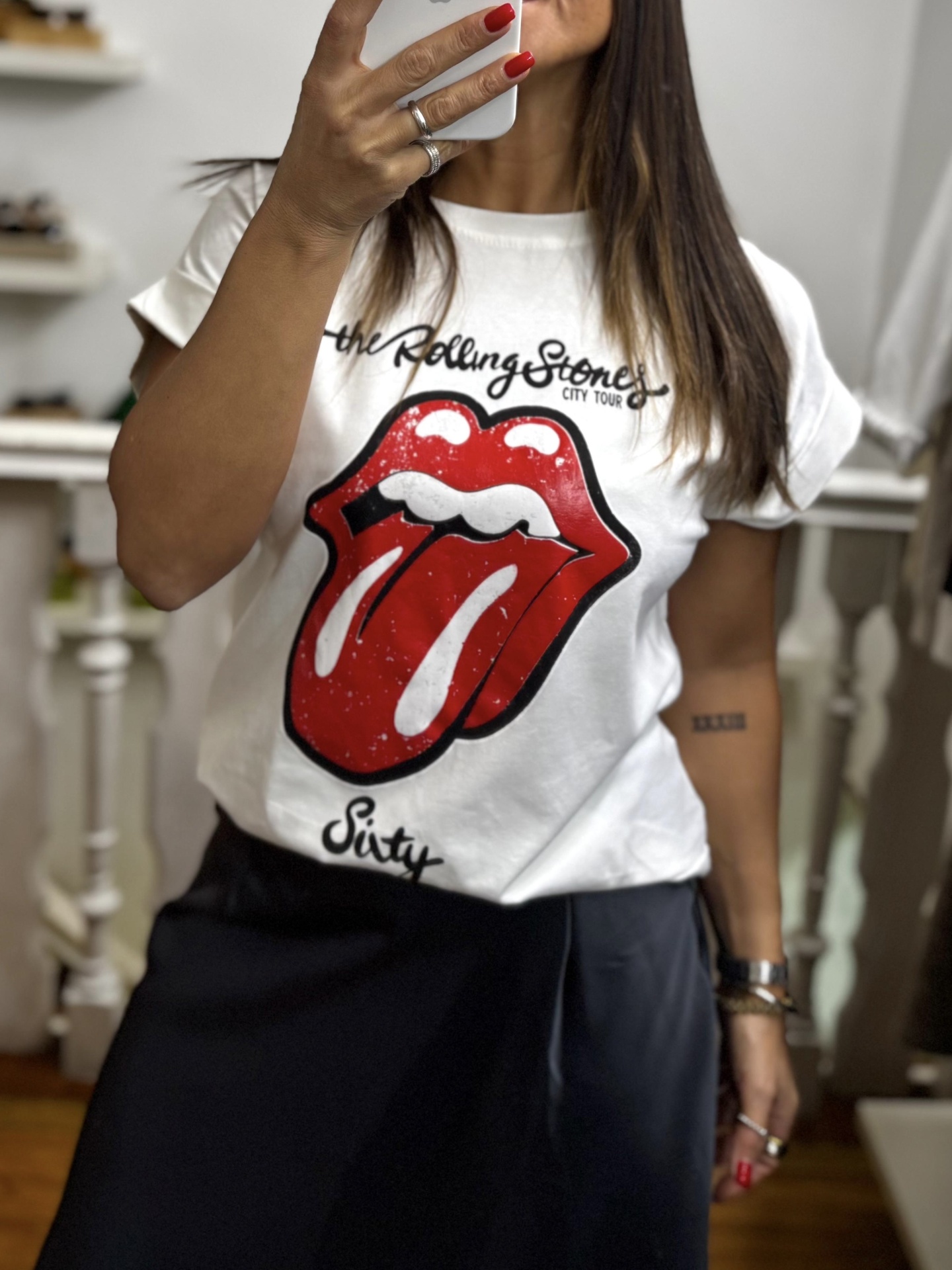 Pessoa vestindo t-shirt branca com estampa dos Rolling Stones e saia escura em ambiente interior