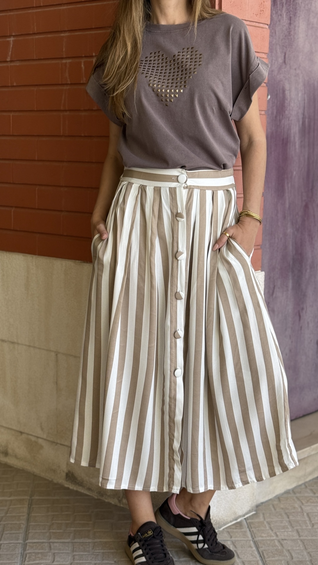 Conjunto de blusa castanha com coração e saia às riscas brancas e castanhas com botões, usar com ténis pretos com riscas brancas.
