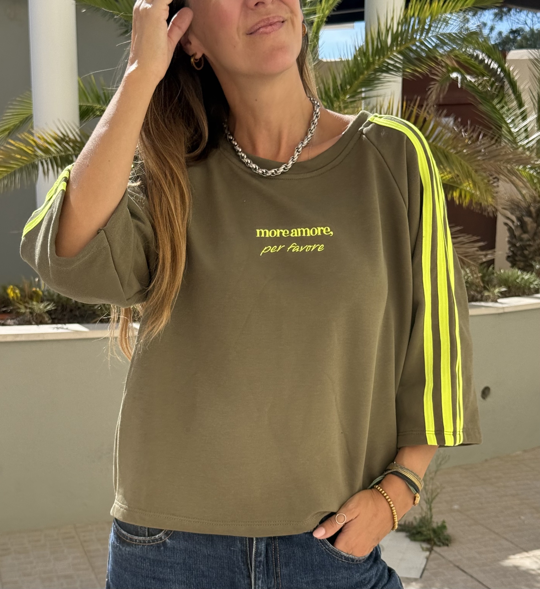 Sweatshirt verde com listas amarelas fluorescentes nas mangas e texto amarelo no peito e calças de ganga azuis