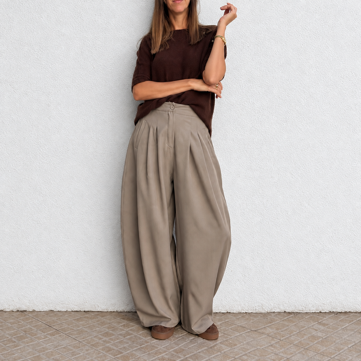 Calças largas bege com pregas, camisola castanha de malha, pulseira dourada e sapatos castanhos