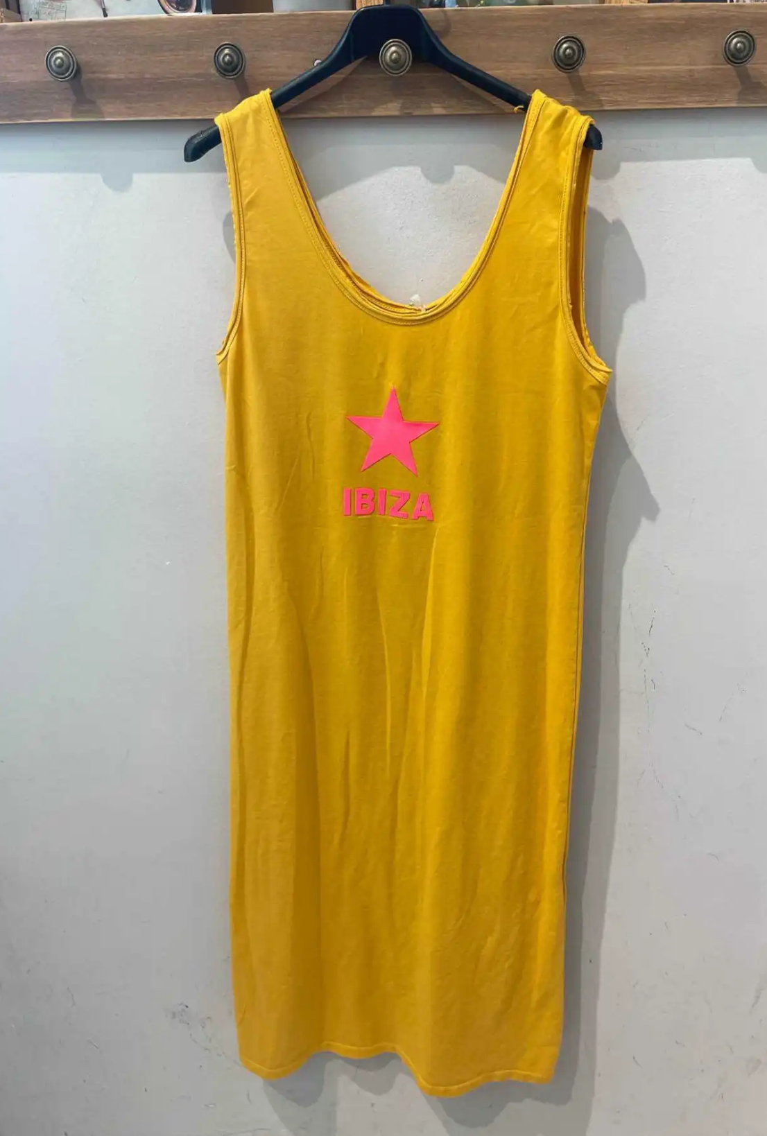 Vestido amarelo com estampa rosa e a palavra IBIZA pendurado