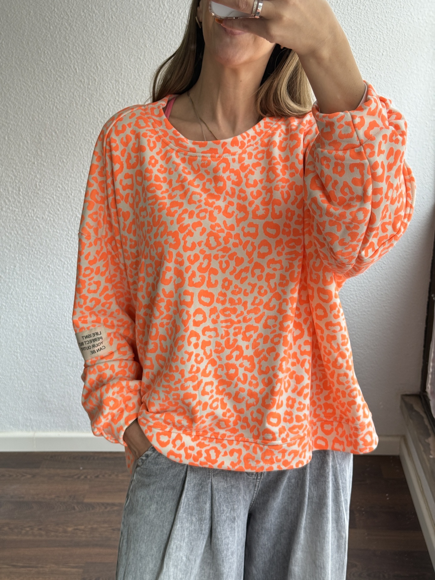 Sweatshirt feminina padrão animal laranja neon com etiqueta no punho sobre calças cinza
