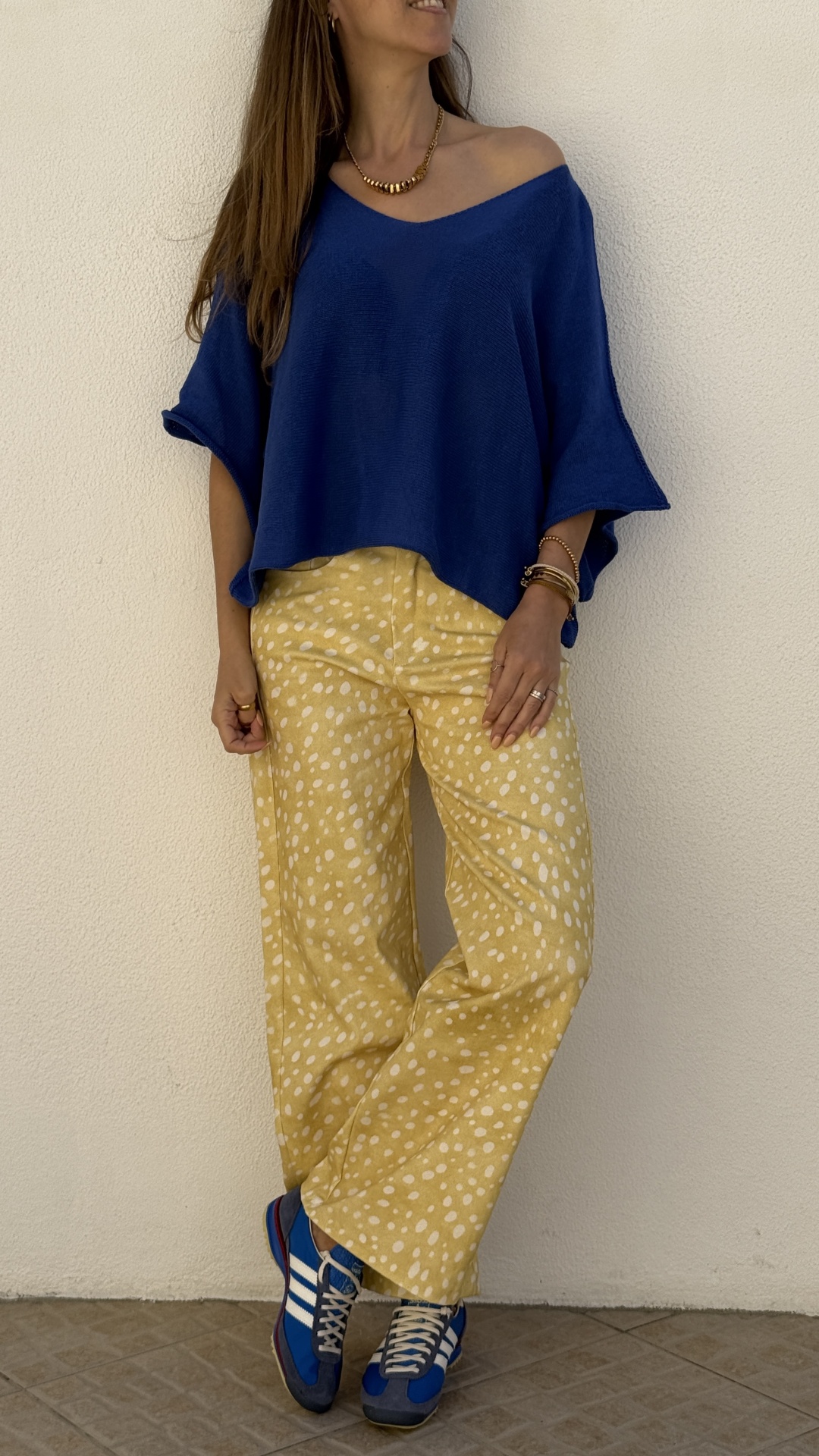 Mulher com camisola azul escura, calças amarelas com manchas brancas e ténis azuis